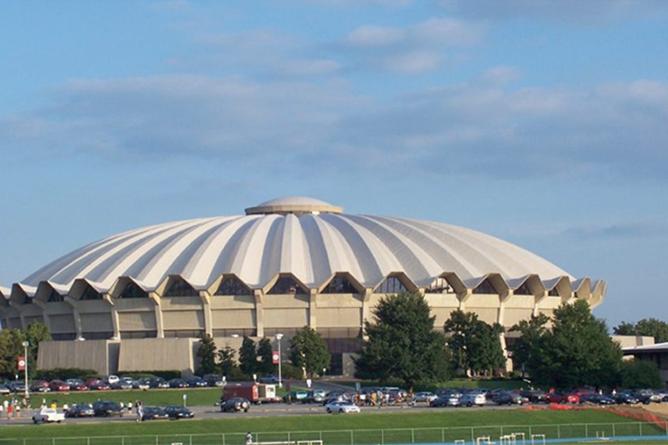 A large stadium with cars parked in front of it.