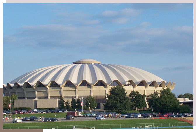 A large stadium with cars parked in front of it.